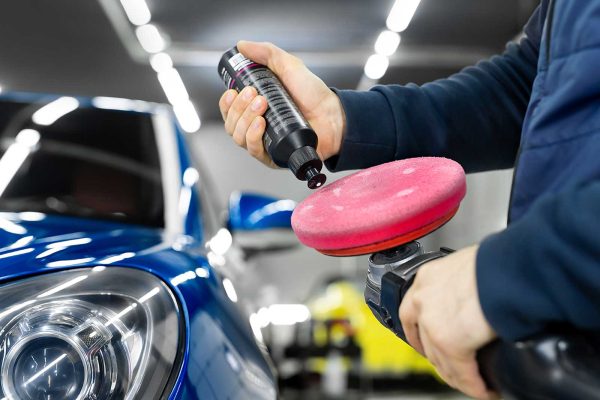 Professional detailing of the car in the auto studio, the master applies paste or wax to the car body polishing machine
