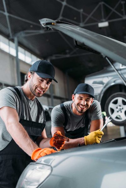 professional smiling auto mechanics repairing car in workshop