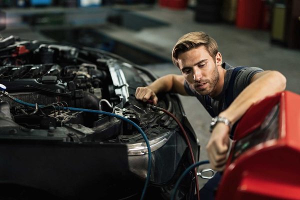 Auto mechanic doing service of car's air conditioning system in repair shop.